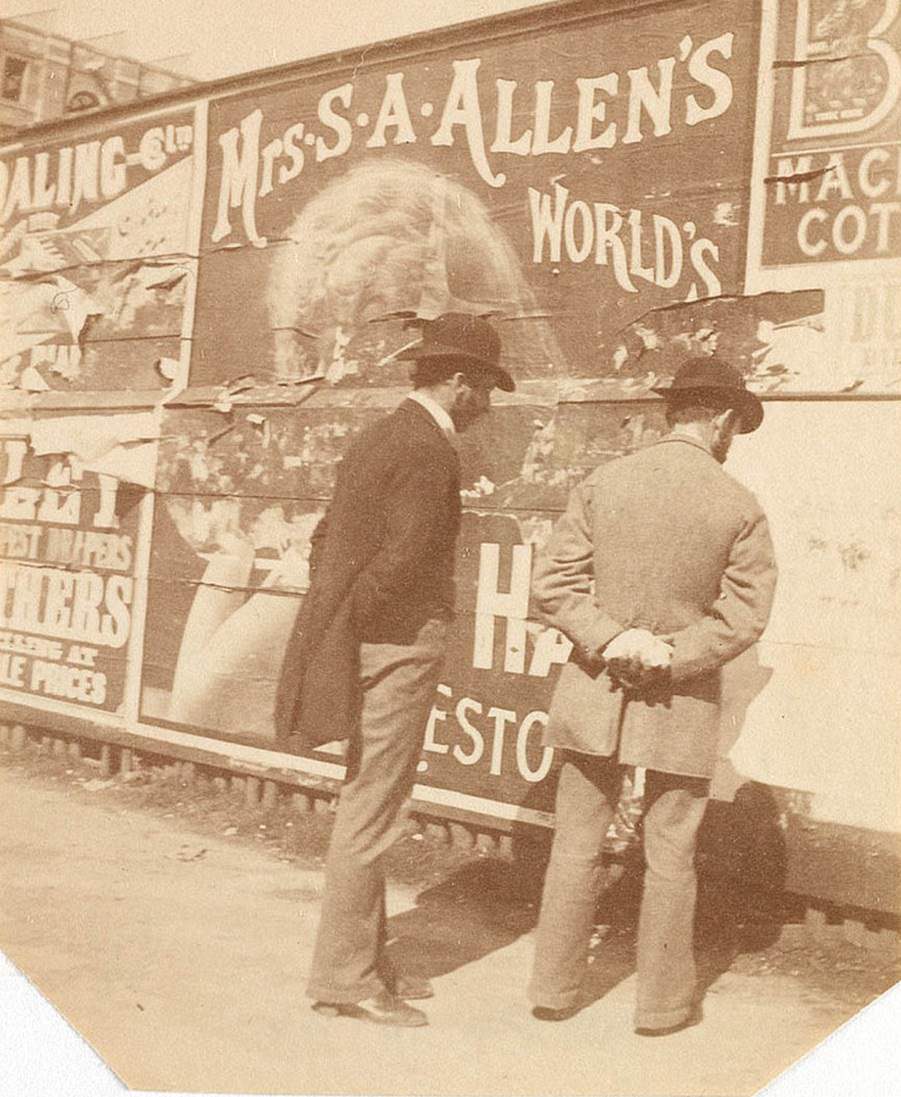 Two men are seen looking at advertisements on a wall in the city circa 1885-1890
