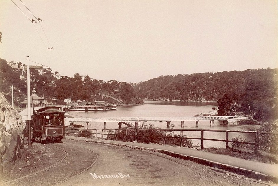 Mosmans Bay circa 1905 shows a tram travelling down a hill and around a corner down towards a wharf, with a passenger ferry parked in the background