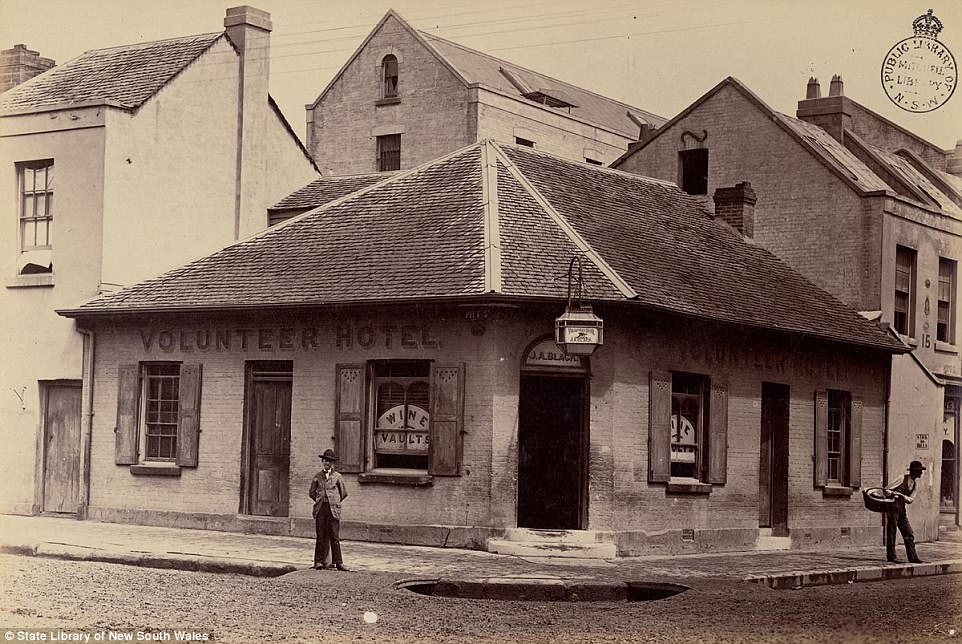 Two men, one holding a basket, are seen standing outside the brick Volunteer Hotel on Pitt Street in Sydney, circa 1870