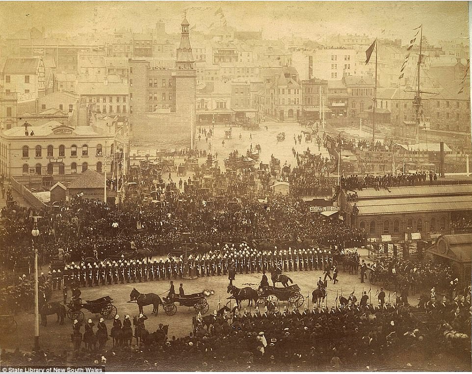 An official parade with horses and carriages is pictured taking place in the city near Sydney Harbour, with ships visible in the background, circa 1885-1890