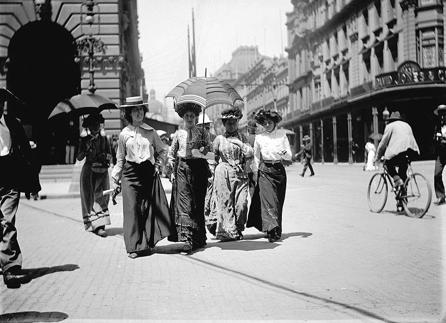 A group of pedestrians on George Street with elaborate bonnets, hats and umbrellas, taken circa 1900