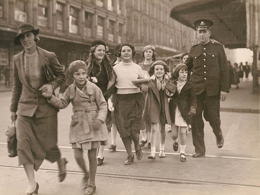 Women and children are seen being escorted across the road by an officer in uniform in Sydney, circa 1940