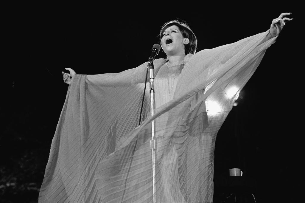 Barbra Streisand dressed in a flowing gown gestures expansively as she performs at a concert in Central Park, 1967