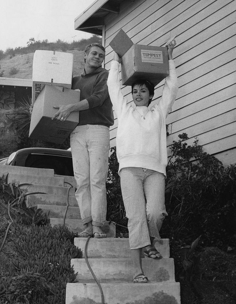 Neile Adams with her hsuband Steve McQueen carrying cardboard boxes down their front steps, circa 1958.