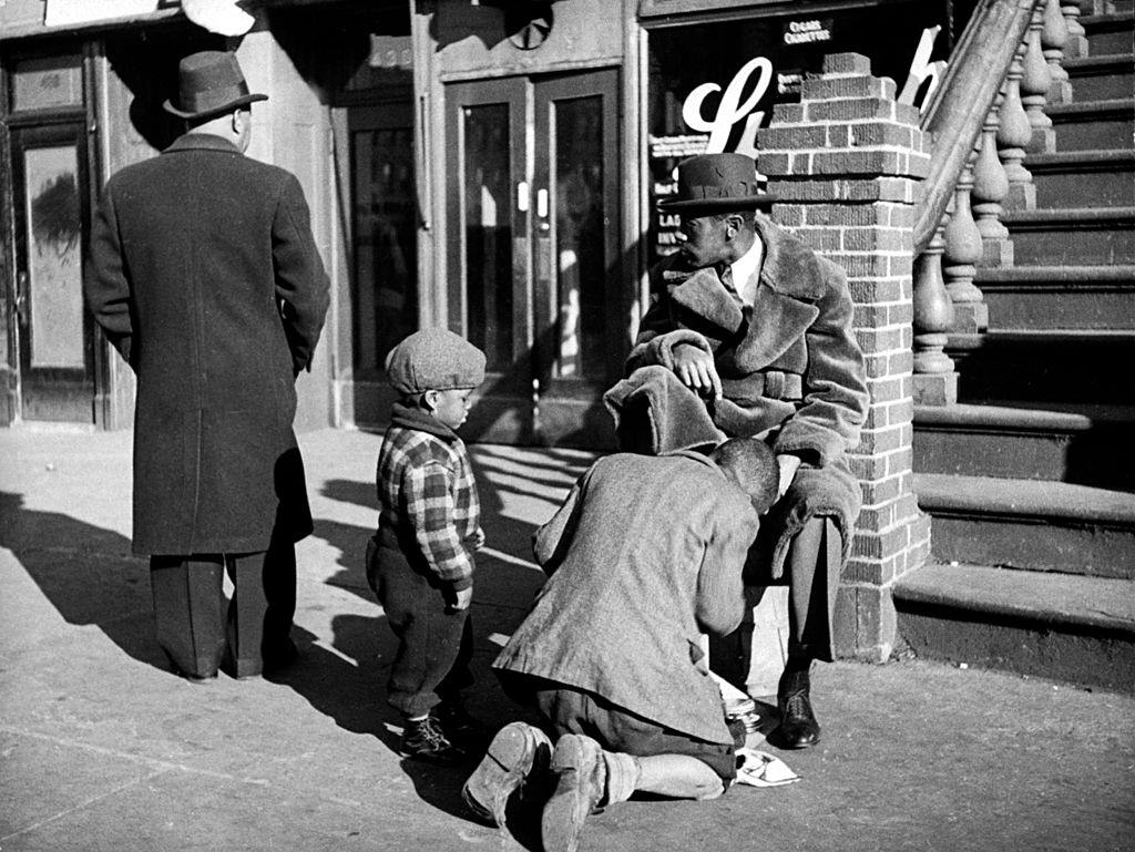 A man getting a shoeshine in Harlem Street, NYC.