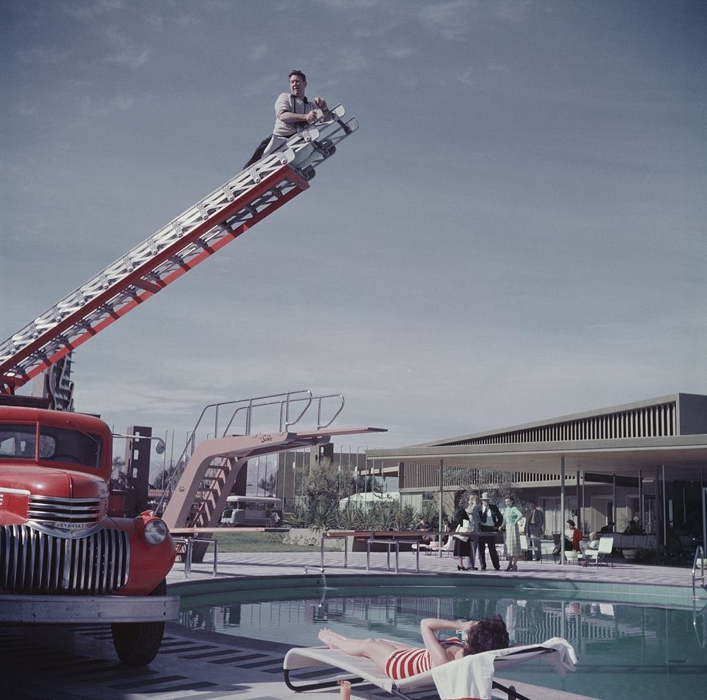 Photographer Slim Aarons photographing film starlet Mara Lane from the top of an extending ladder by the swimming pool at Sands Hotel, Las Vegas, 1954.