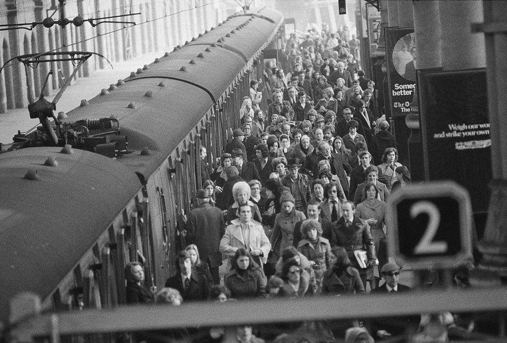 Commuters and passengers walking along a platform at Liverpool Street Station, 1976.