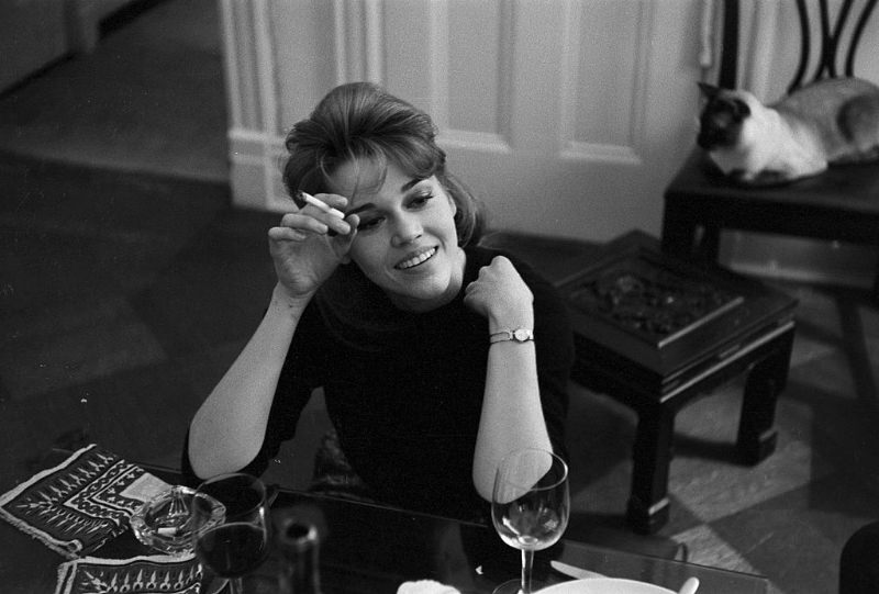 Jane Fonda smoking a cigarette at the dinner table.