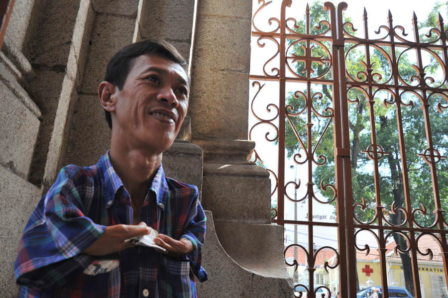 A man begs for money outside of a cathedral. He was born with a deformed arm because of Agent Orange, and it makes it nearly impossible for him to find work.