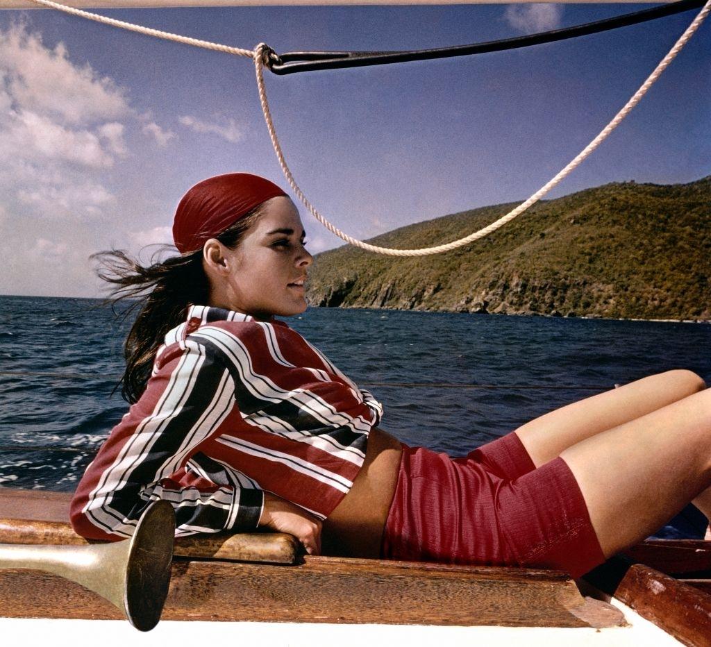 Ali MacGraw reclining on a sailboat modelling a striped shirt and long shorts, 1967.