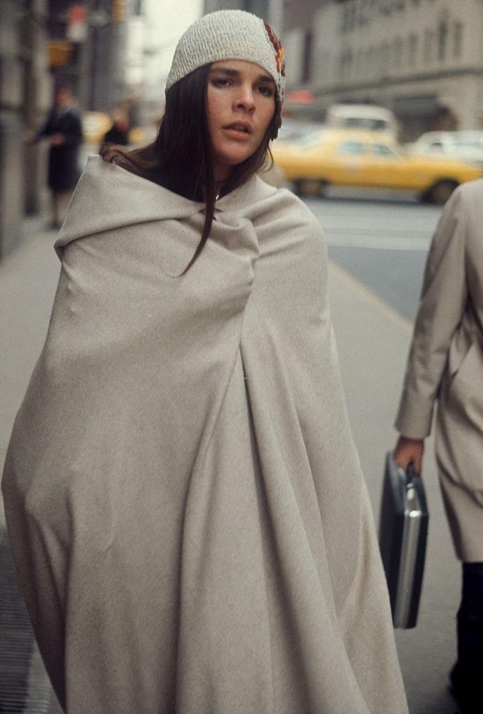 Ali MacGraw wrapped in a blanket walking on the street, 1970.