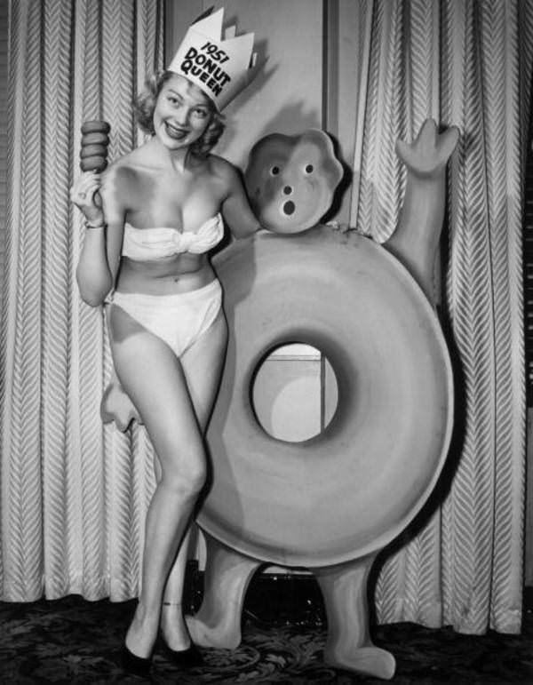 Donut Queen Kris Nodland, wearing high heels and a bikini, poses with donuts and the Gingerbread Donut Boy at the Governor Clinton Hotel in New York, 1951.