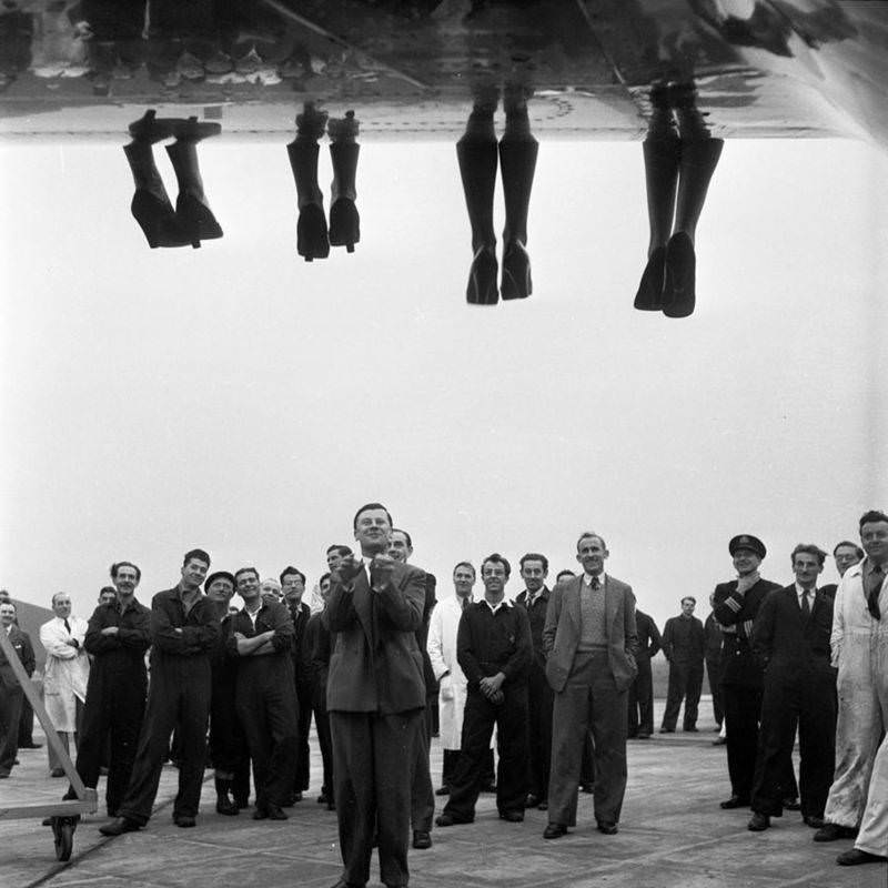 The legs of contestants being judged in a Miss World beauty pageant dangle over the side of a plane while staff stands below, England, 1953.