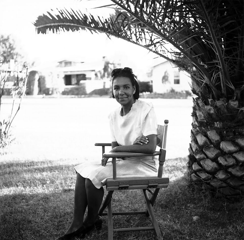 African American woman sitting in a folding chair under a palm tree.