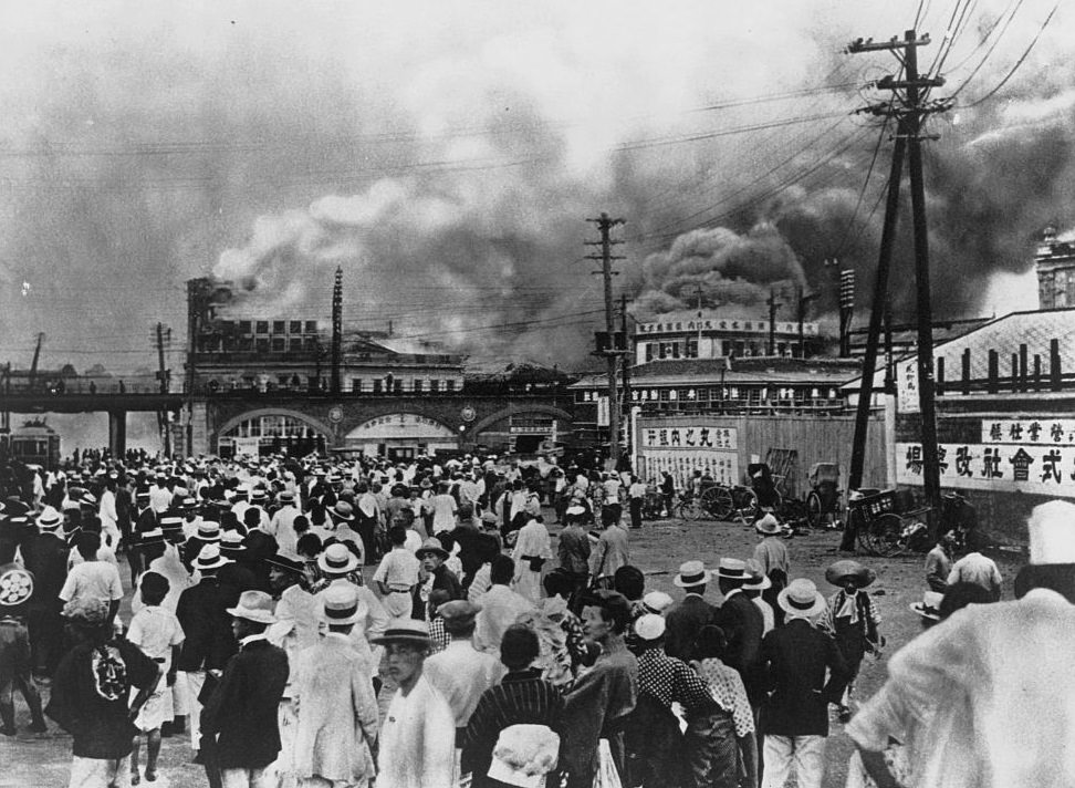 A crowd of people watch as buildings smolder after the earthquake in Tokyo, Japan. September 1, 1923.