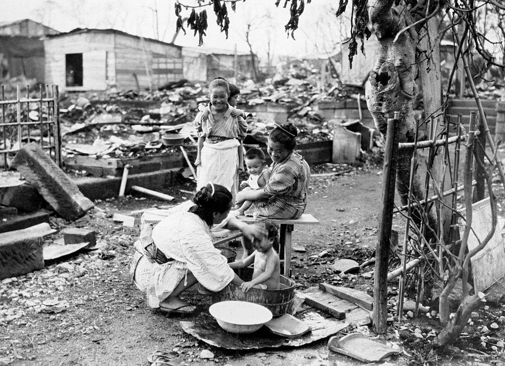 Egy csecsemő fürdik a romok között, melyeket a szeptemberi Yokohama, Japán, 1923. november 7-i Yokohama földrengés után maradtak meg.