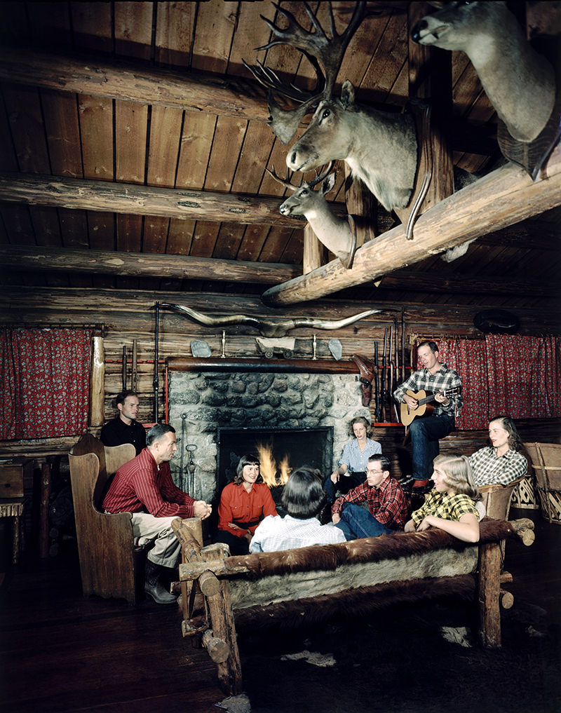 Guests sitting around fireplace and listening to live music at Bearpaw Dude Ranch. Jack Huyler, son of owner, is playing guitar. Jackson Hole, Wyoming, 1948.