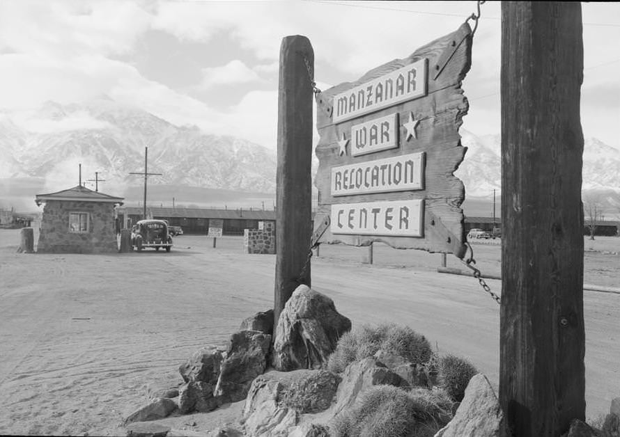 Wooden sign at entrance to the Manzanar War Relocation Center with a car at the gatehouse in the background.