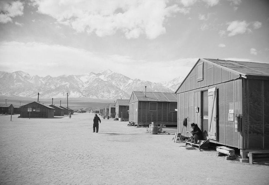 Rows of camp housing, covered on the outside with tarpaper, snow-covered mountains in the distance.