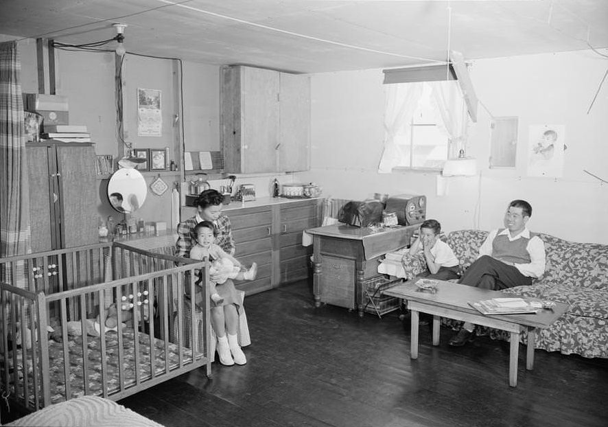 Family seated in combined living room and kitchen area with playpen.