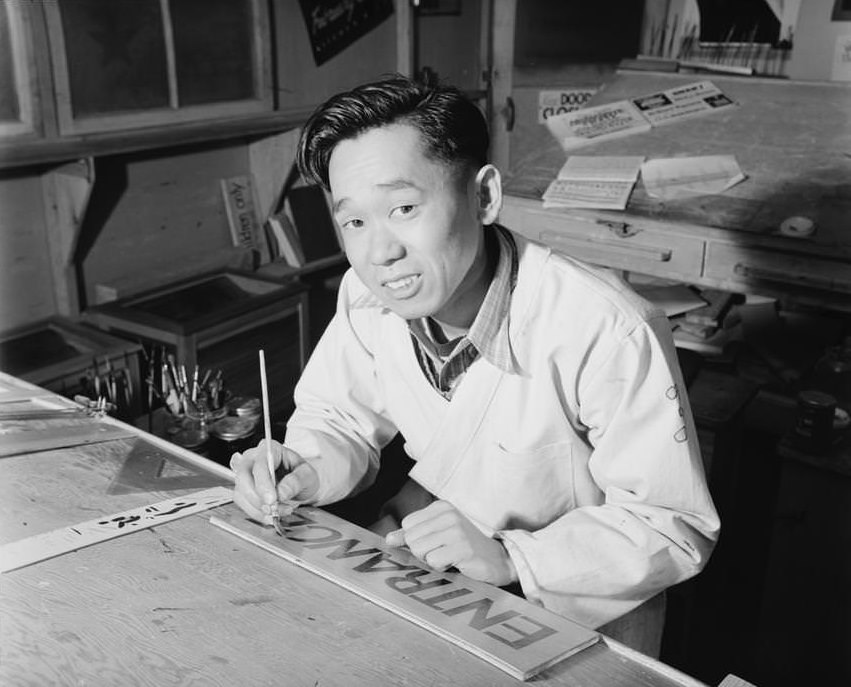 Akio Matsumoto, half-length portrait, seated at desk, facing front, painting sign.