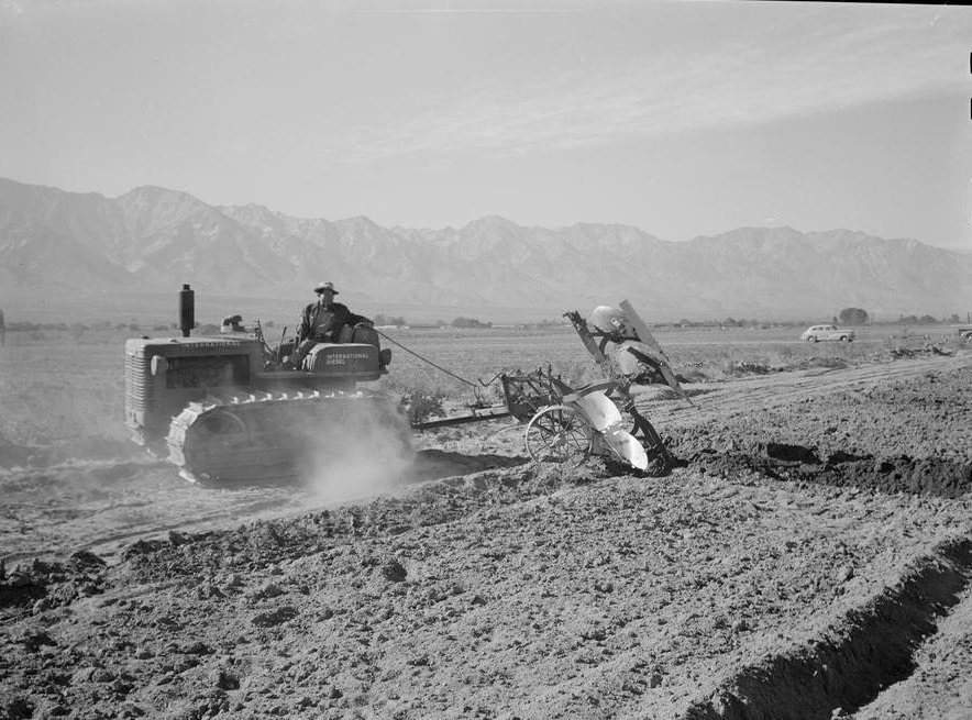 A tractor pulls a plow through a field, mountains in the background.