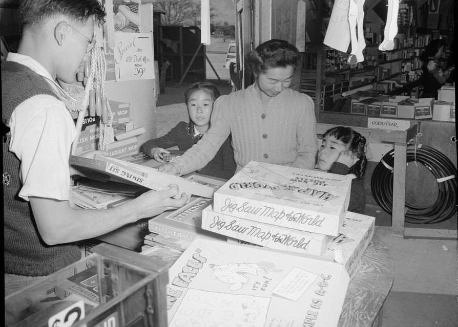 Mrs. Yaeko Nakamura looks at puzzles with her daughters, Louise Tami Nakamura and Joyce Yuki Nakamura in a store with assistance from clerk, Fred Moriguchi.