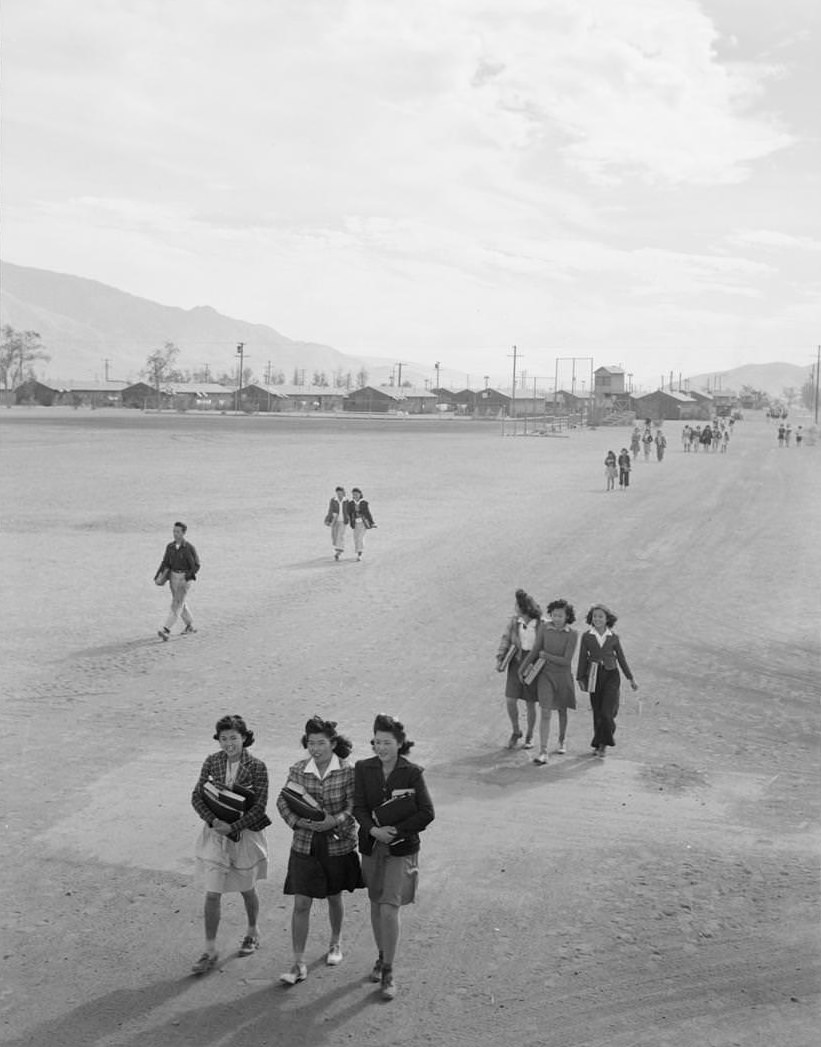 Teenagers walking along street, most carrying books.