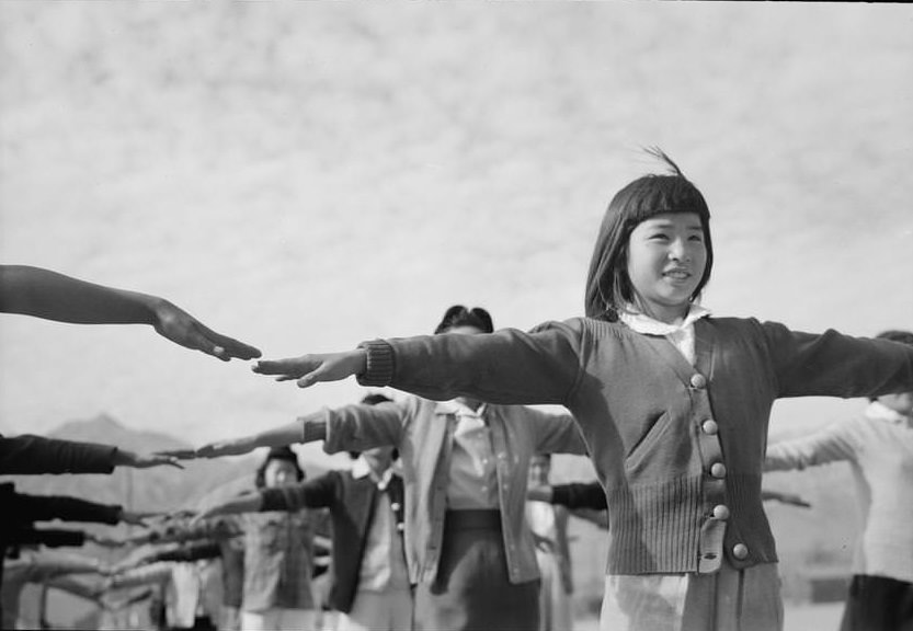 Group of girls standing in line formation, each one reaching both of her arms straight out to the side.