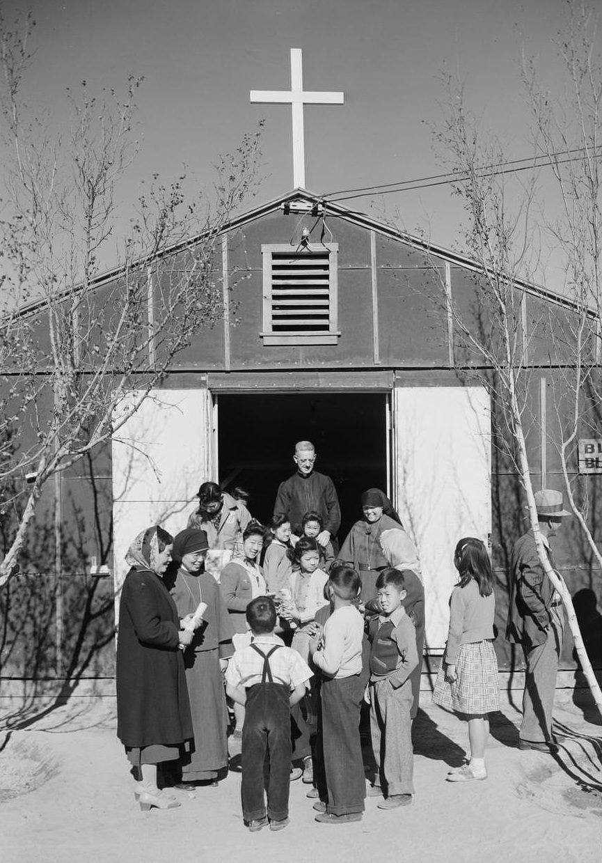 Group of people gathered outside the front of a building with a cross on the roof.