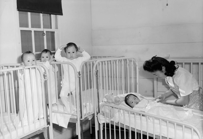 Nurse tending four infants in cribs.