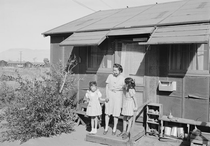 Standing on the step at the entrance of a dwelling, left to right: Louise Tami Nakamura, holding the hand of Mrs. Naguchi, and Joyce Yuki Nakamura.
