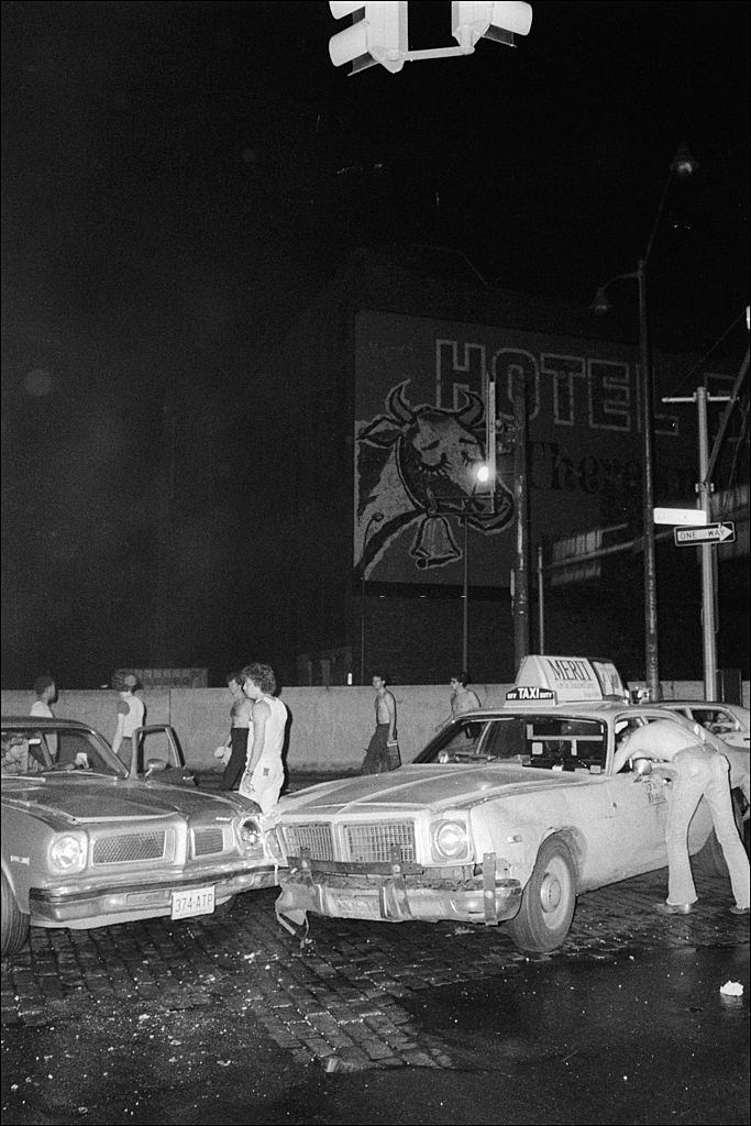 Az áramszünet alatt a szemlélő gyalogosok állnak körül egy autó és egy taxi közötti közlekedési baleset körül, New York City, 1977. július 13..