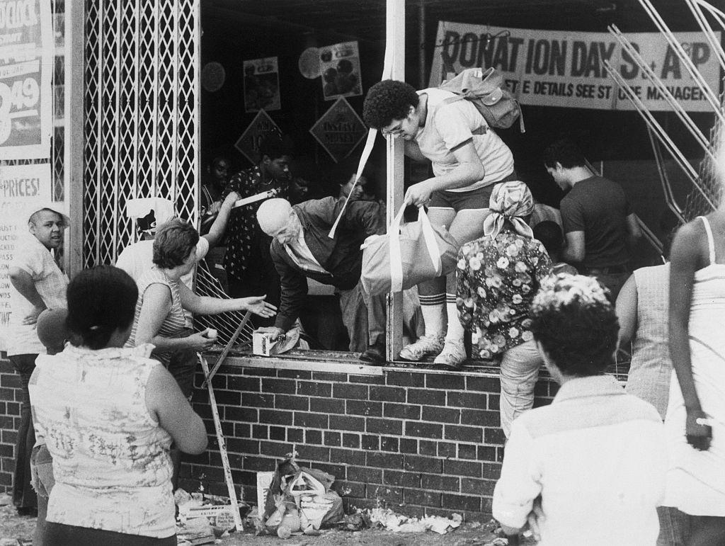 Looters, young and old, leave an A & P supermarket at Ogden Avenue and 166th Street in the Bronx through a broken window, New York, New York, 1977.