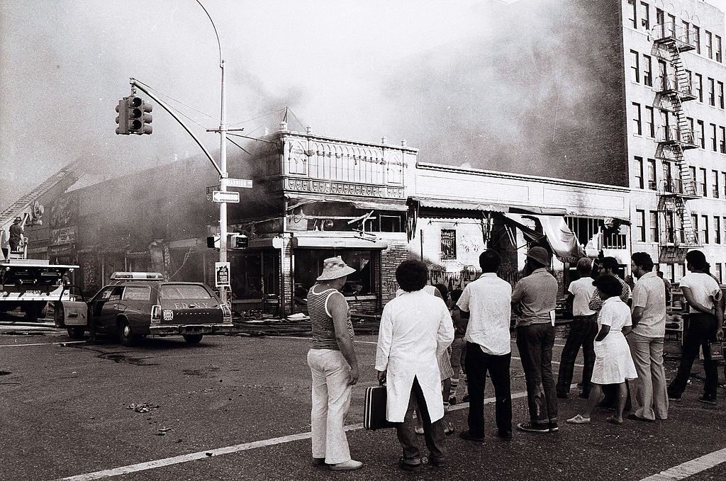 People look on on as firemen put an end to arsonist's handiwork on Marmion Ave, New York City, July 13, 1977.