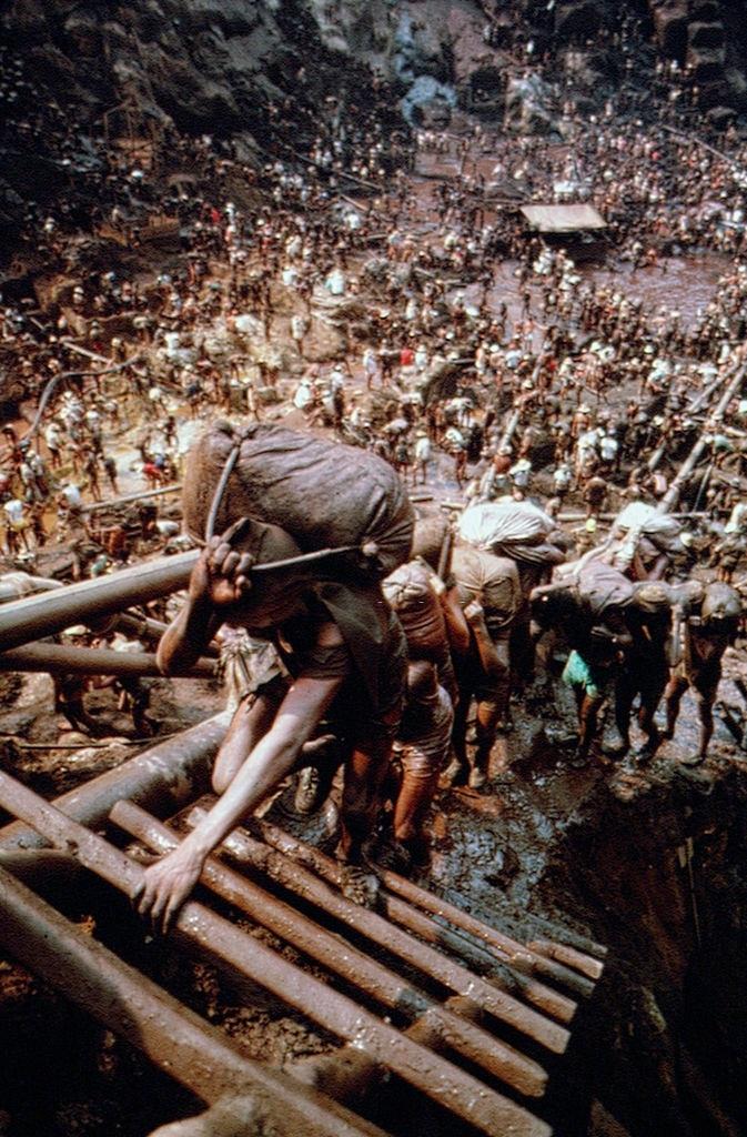 Hundreds of workers carrying bags from the pit up the slopes in Serra Pelada Gold Mine, Brazil, 1980s.