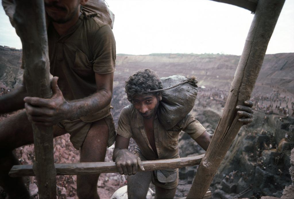 Mine workers use a wooden ladder to carry out 40-pound bags of ore, Serra Pelada, Brazil.