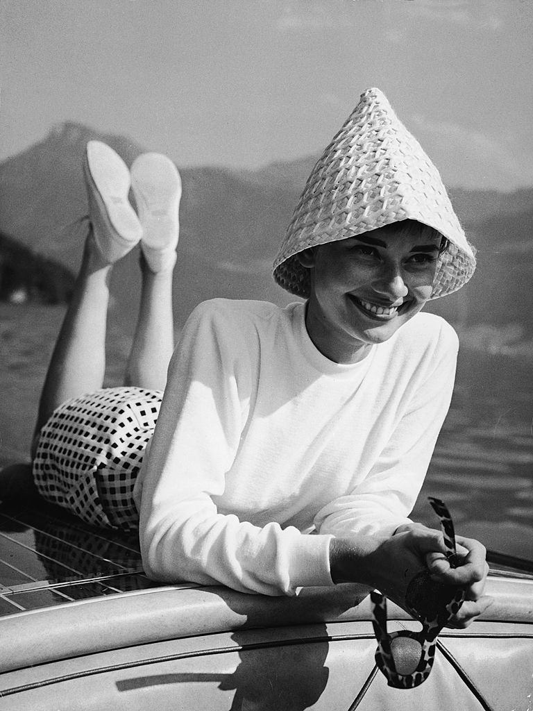 Audrey Hepburn wears a peculiar hat and lies on the back of a motorboat on a lake in Switzerland, early 1950s.