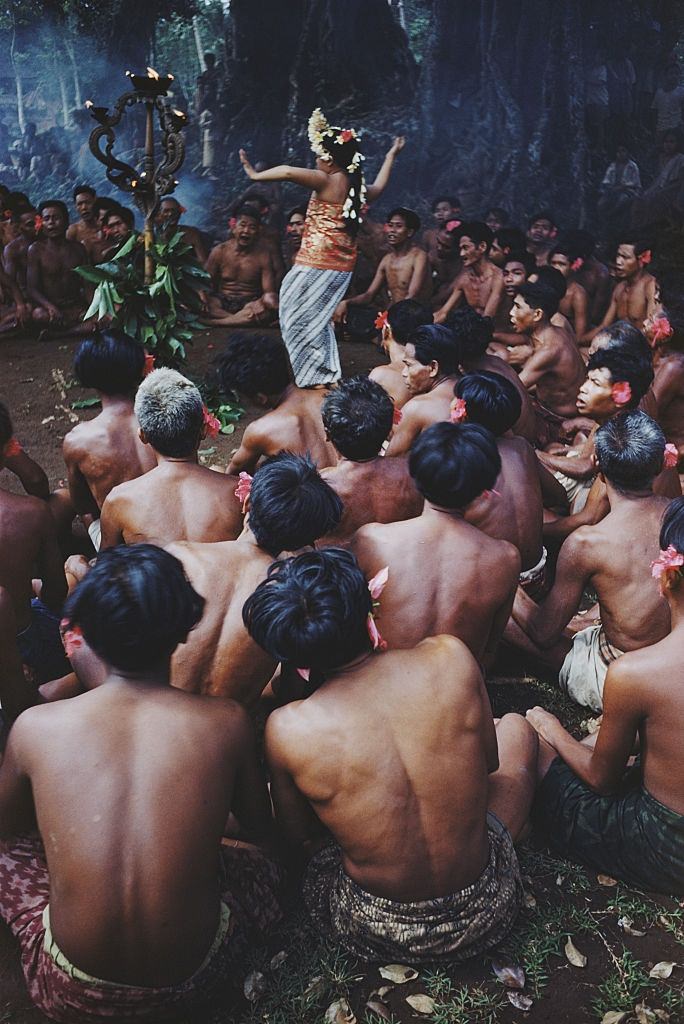 Stripped to the waist Balinese men watch a woman dance round a 'totem', 1956.