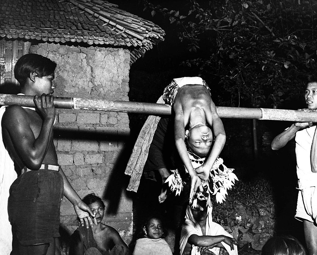A Balinese trance dancer bends backwards over a pole held up by two boys. The spirit of a god is said to have entered her in her hypnotised state, 1958.