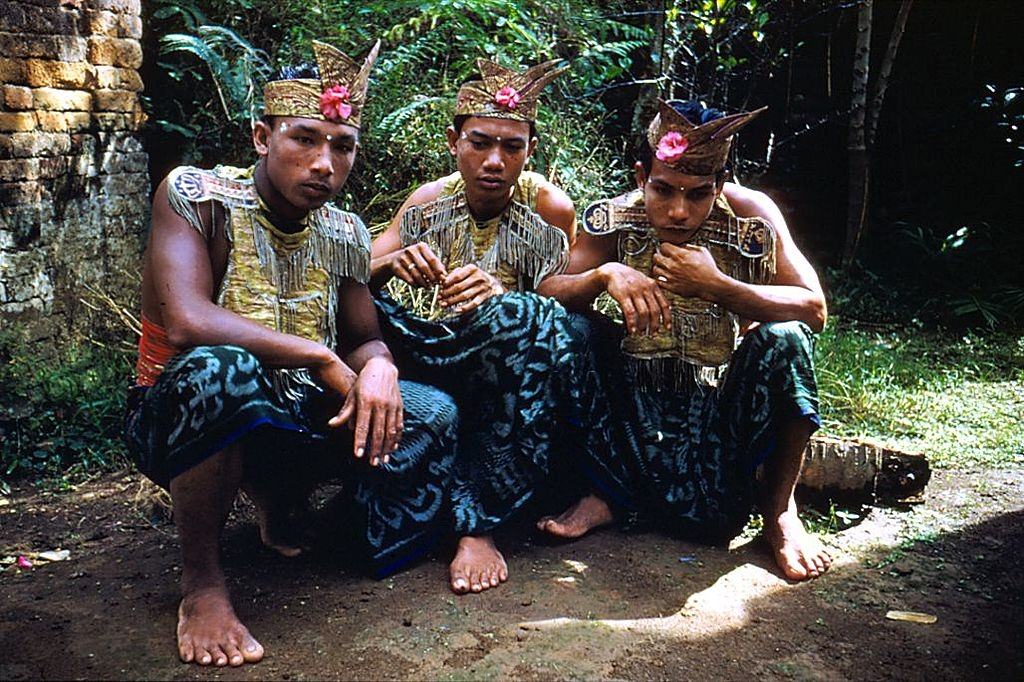 Three bare-footed male Balinese dancers in costume pose for the camera during a rest break, Bali, 1956.