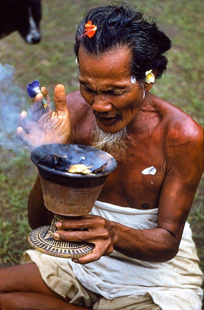 A Balinese man holds a cup and inhales fumes from the smoking ashes within, 1956.