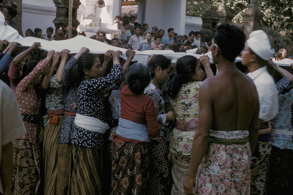 People holding a long white piece of clothe during a cremation, Bali, 1958.