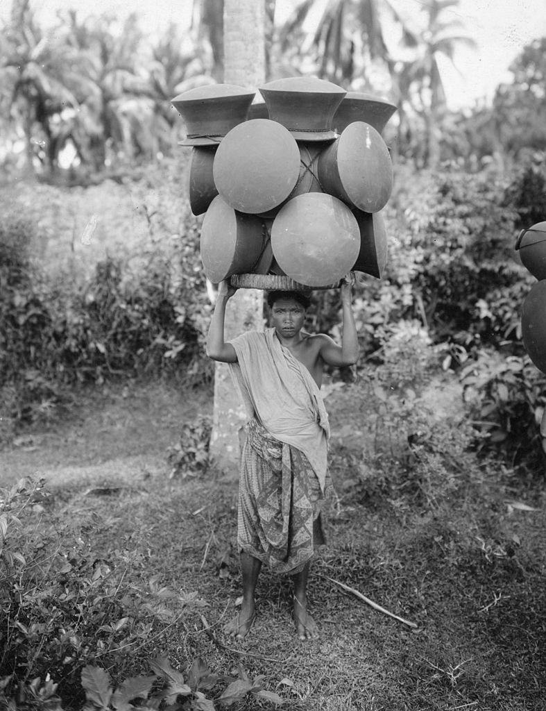 A woman balancing hand made clay pots on her head to carry them hundreds of miles to market. Bali, 1955