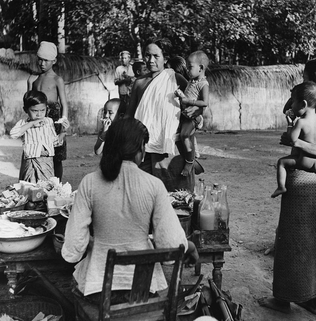 Women and children gathered around a street food stall in Bali, Indonesia, 1951.