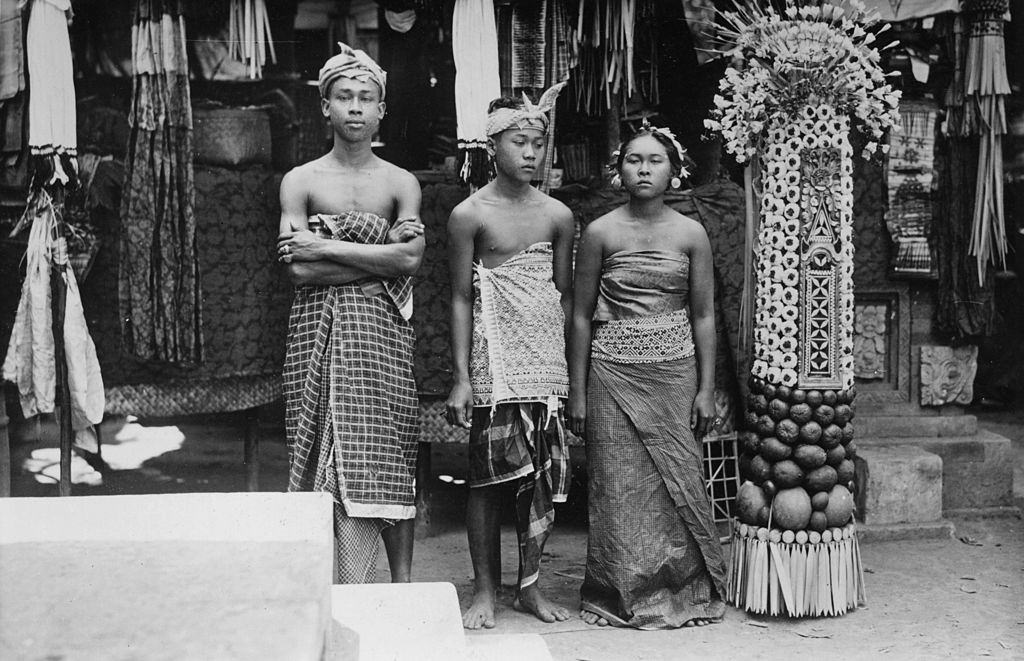 Three young Indonesians standing by a votive made from fruit and flowers in Bali, 1951.