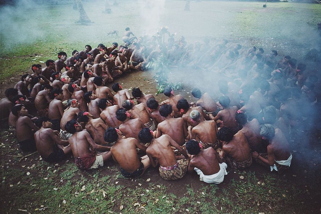 A deep circle of Balinese men sway in unison in a 'kecak' dance as smoke from burning green leaves drifts over them, Bali, 1956.