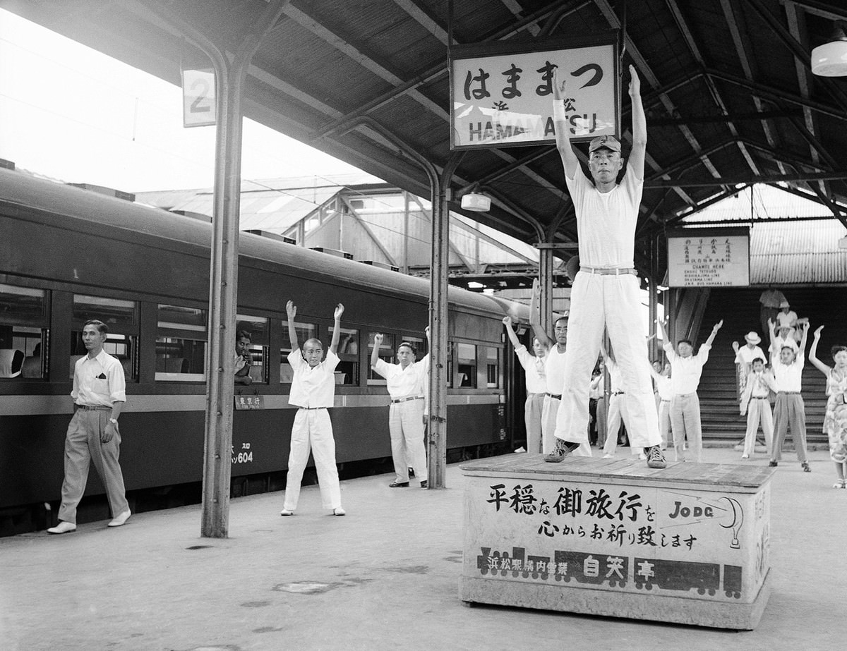 Passengers on a train traveling from Tokyo to Osaka go through three minutes of calisthenics under leadership of a drill master, during a five-minute stopover at Hammamatsu on August 27, 1952.