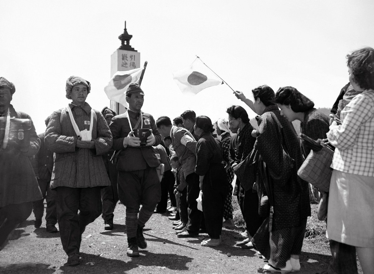 Women greet repatriated Japanese soldiers, formerly prisoners of war, on April 26, 1950. The men bear the ashes of their friends who died during their imprisonment.