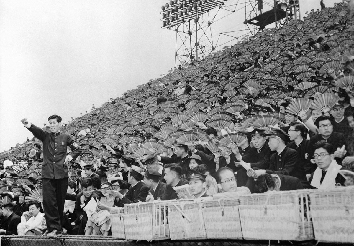 Spectators equipped with fans watch a baseball game between Waseda and Keio Universities at Meiji Park, Tokyo, on June 1, 1954.